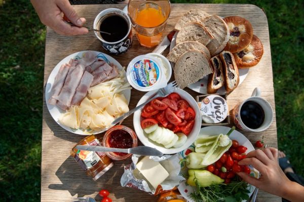 Enjoy a delightful outdoor brunch with bread, cheese, cold cuts, coffee, and fresh vegetables.