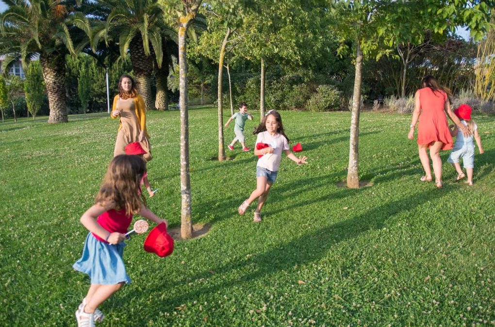 Kids and adults enjoy playing together in a lush, sunny park setting.