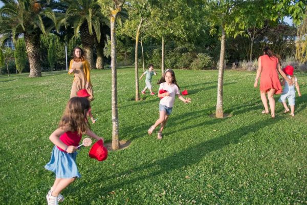 Kids and adults enjoy playing together in a lush, sunny park setting.